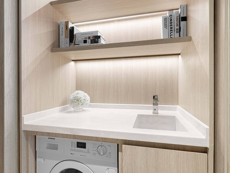 A compact laundry room with a washing machine, a sink, and a shelf with books.