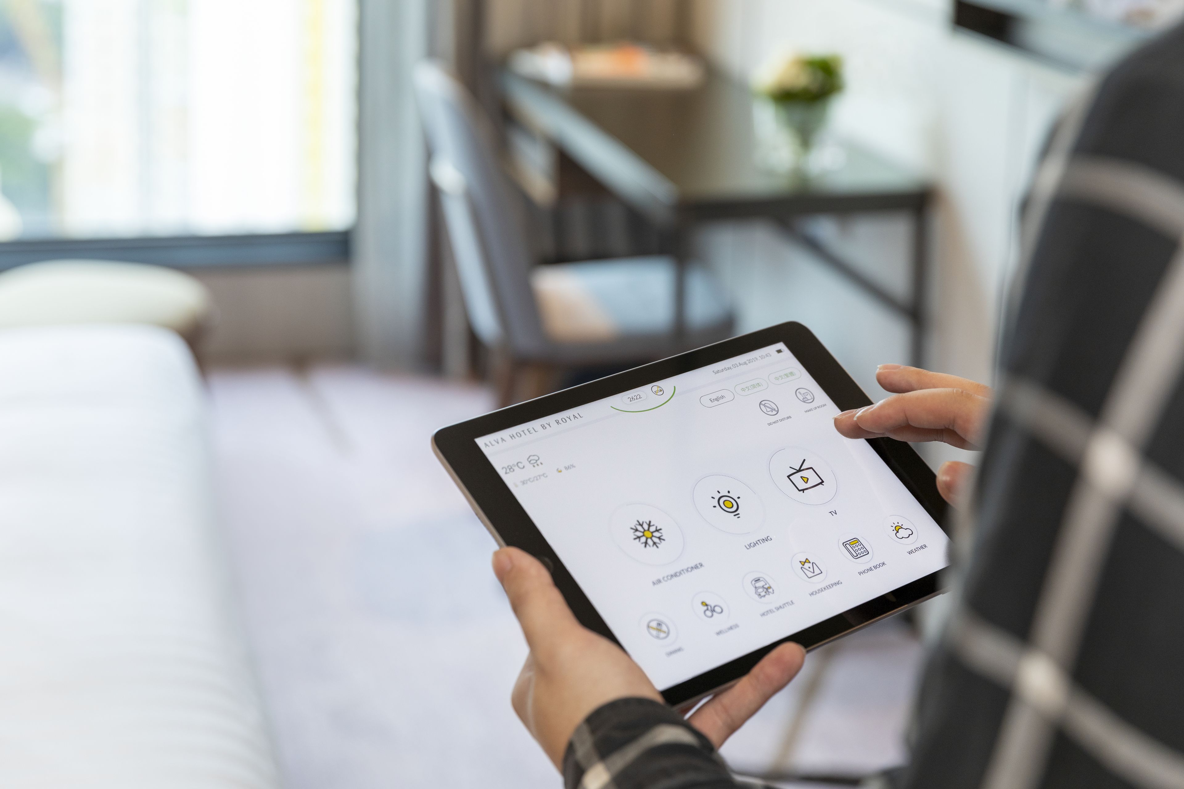 A person holding a tablet displaying a hotel app interface with options for air conditioning, lighting, and other amenities.