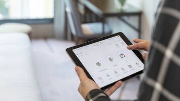 A person holding a tablet displaying a hotel app interface with options for air conditioning, lighting, and other amenities.