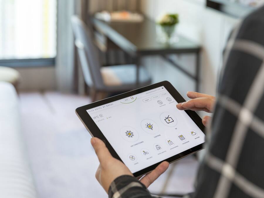A person holding a tablet displaying a hotel app interface with options for air conditioning, lighting, and other amenities.