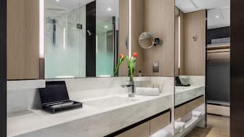 Un baño moderno con un espejo grande, un lavamanos de mármol y un neceser negro.
