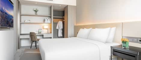 Una habitación de hotel moderna con una cama grande, un escritorio con una silla, un armario y un televisor en la pared.