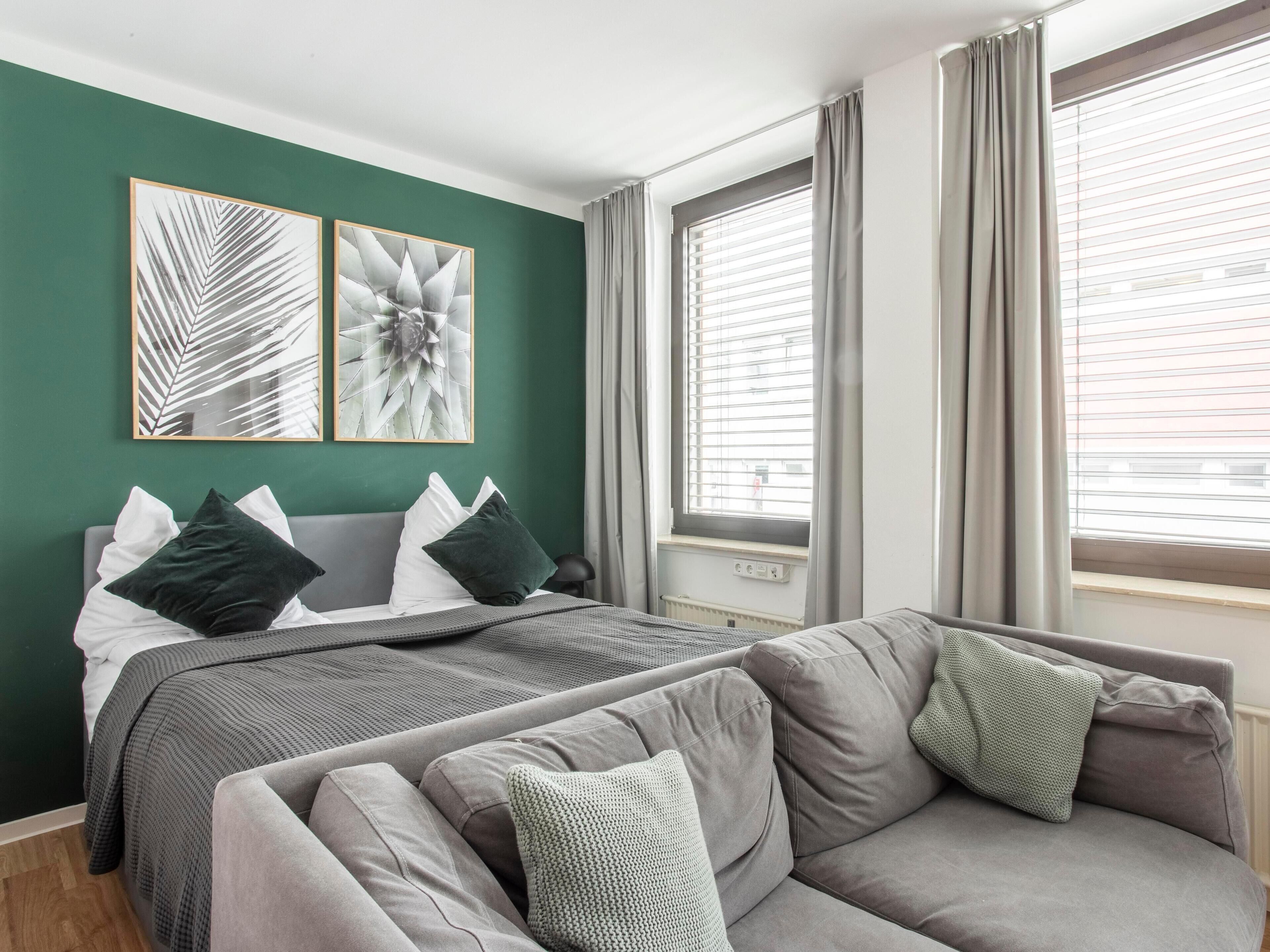 Ein modernes Schlafzimmer mit einem Bett, zwei grauen Sofas und Kunstwerken an der Wand.