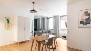 A modern living space with a wooden dining table, grey chairs, a sofa, and a hanging pendant light.