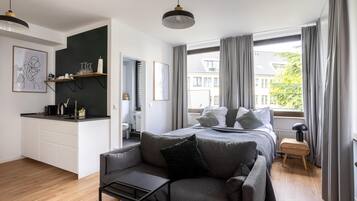 Un dormitorio moderno con cama, sofá, una mesita y vistas de la ciudad a través de amplias ventanas.