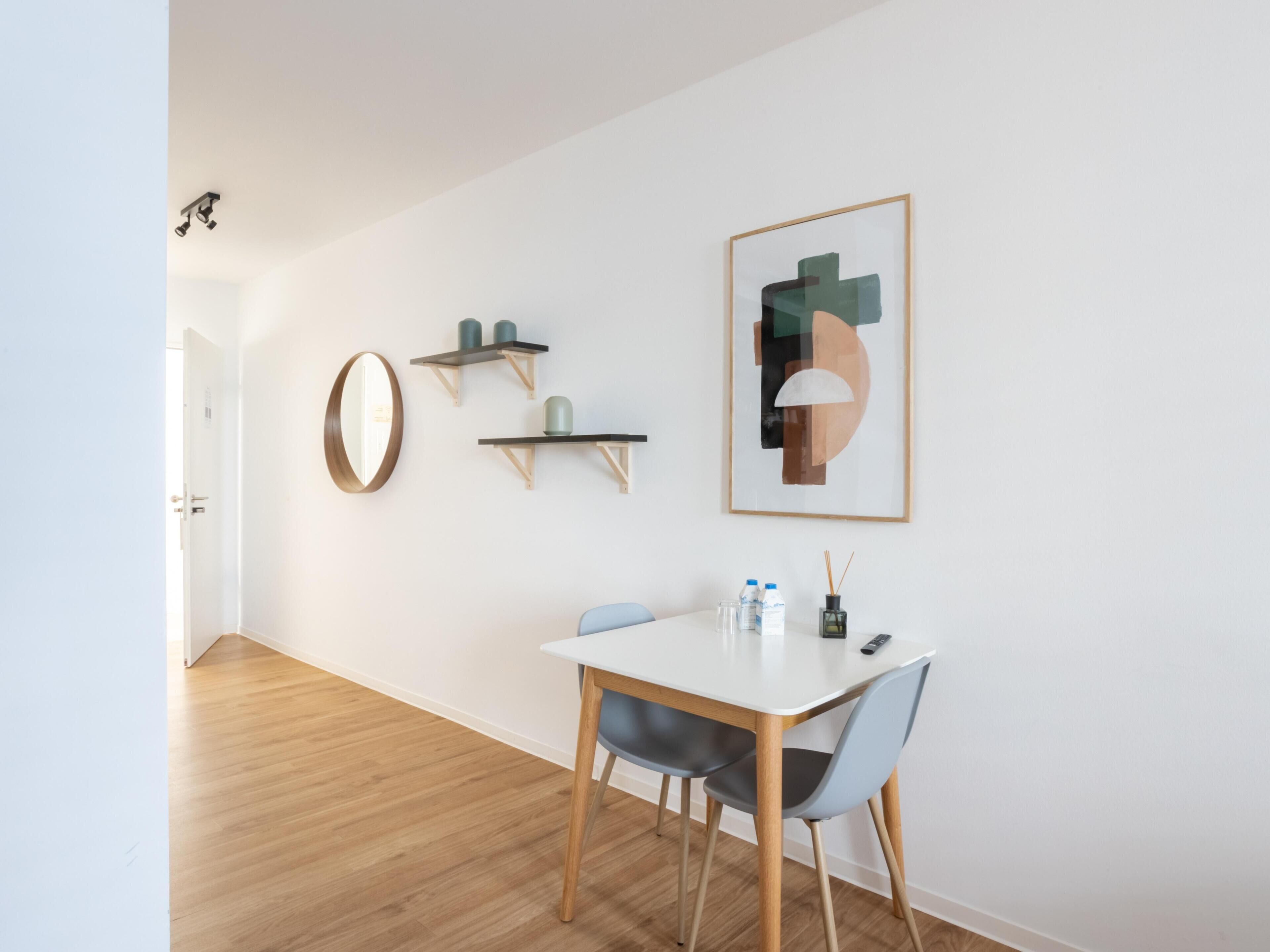 Un espace repas moderne avec une table blanche, deux chaises et un tableau abstrait encadré accroché au mur.