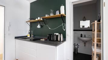 A modern kitchen with a dark green accent wall, wooden shelves, a built-in sink, and a compact layout.