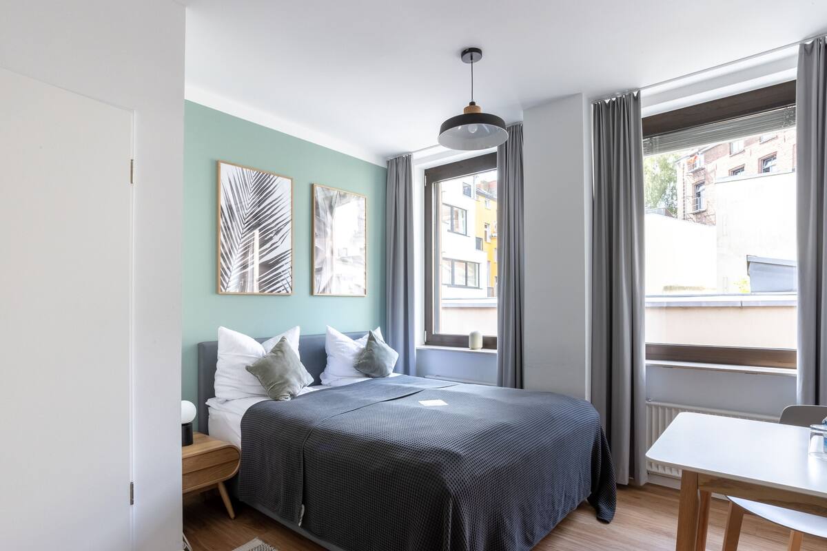 Een moderne slaapkamer met een bed, nachtkastje en een raam met gordijnen.