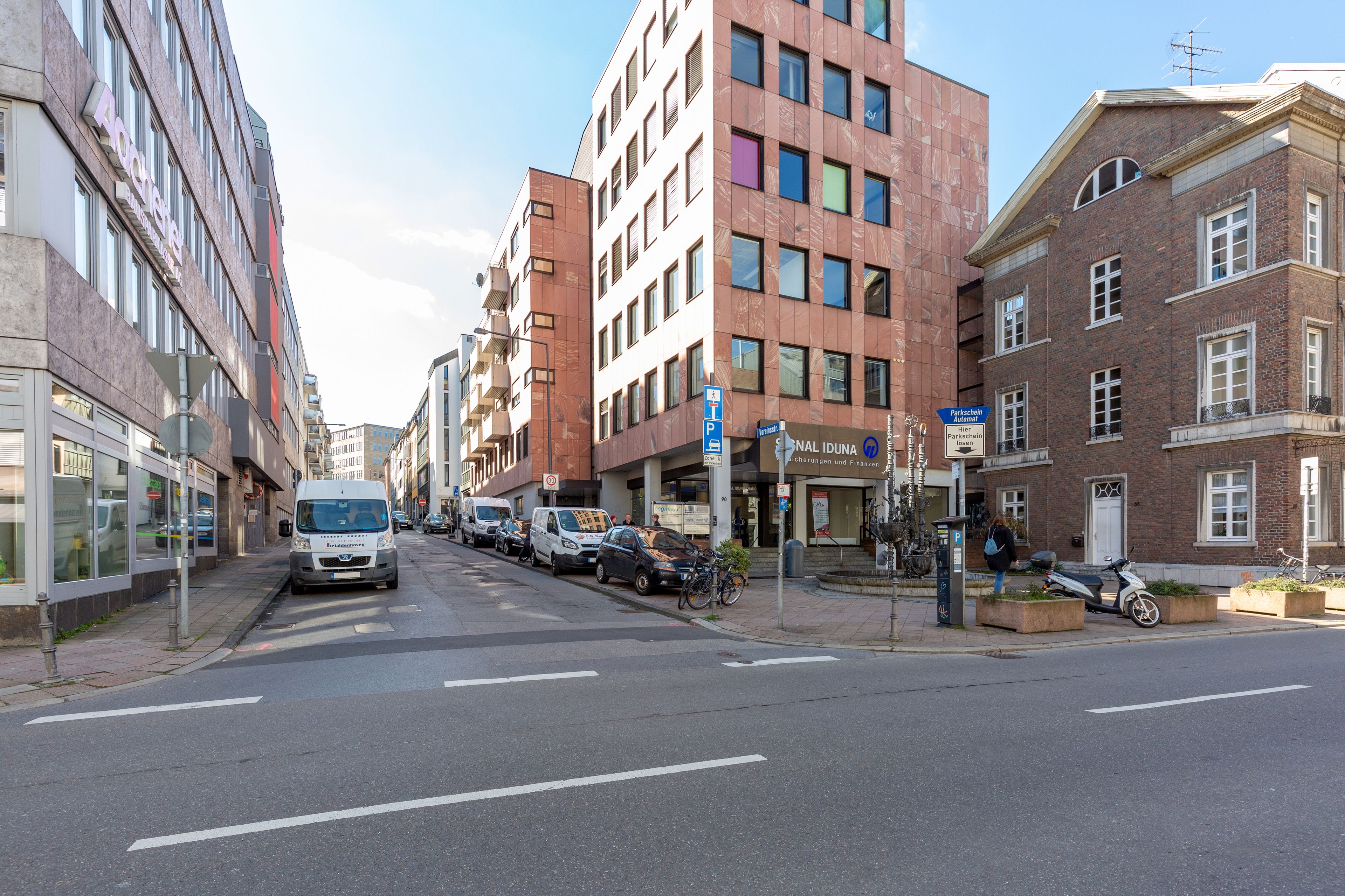 Straßenansicht mit Gebäuden, parkenden Autos und einem Fahrrad.