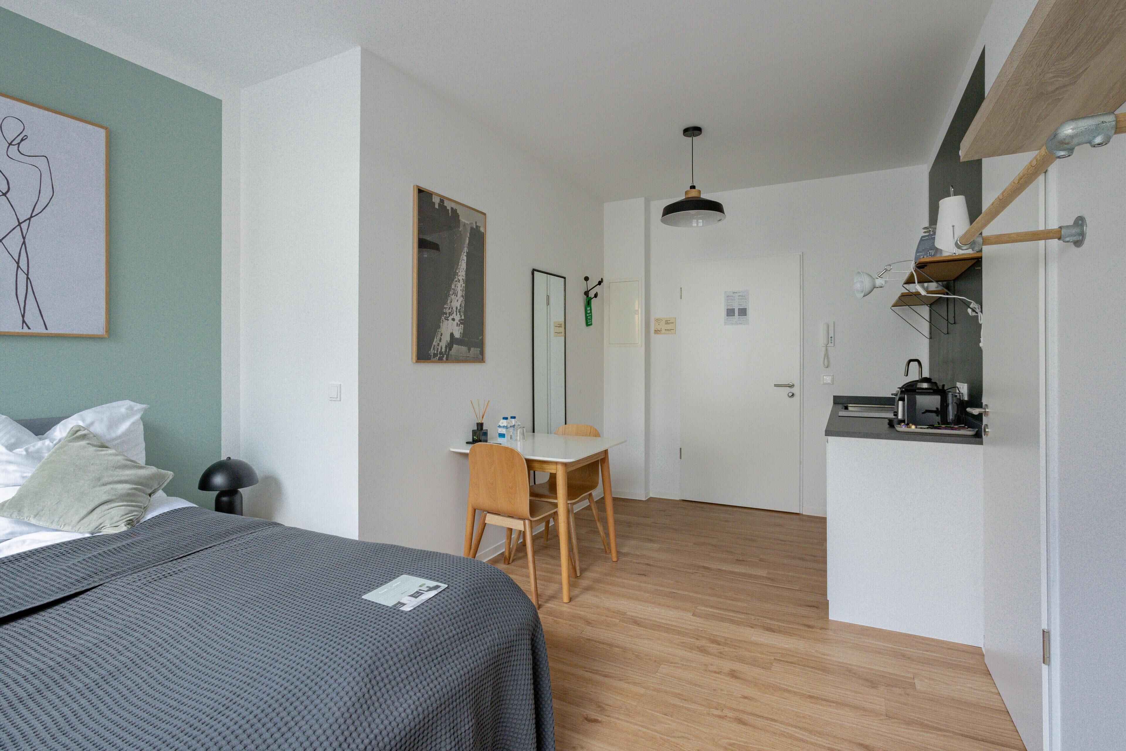 Habitación con una cama, un escritorio y una silla. Se ve una puerta que da a otra habitación.