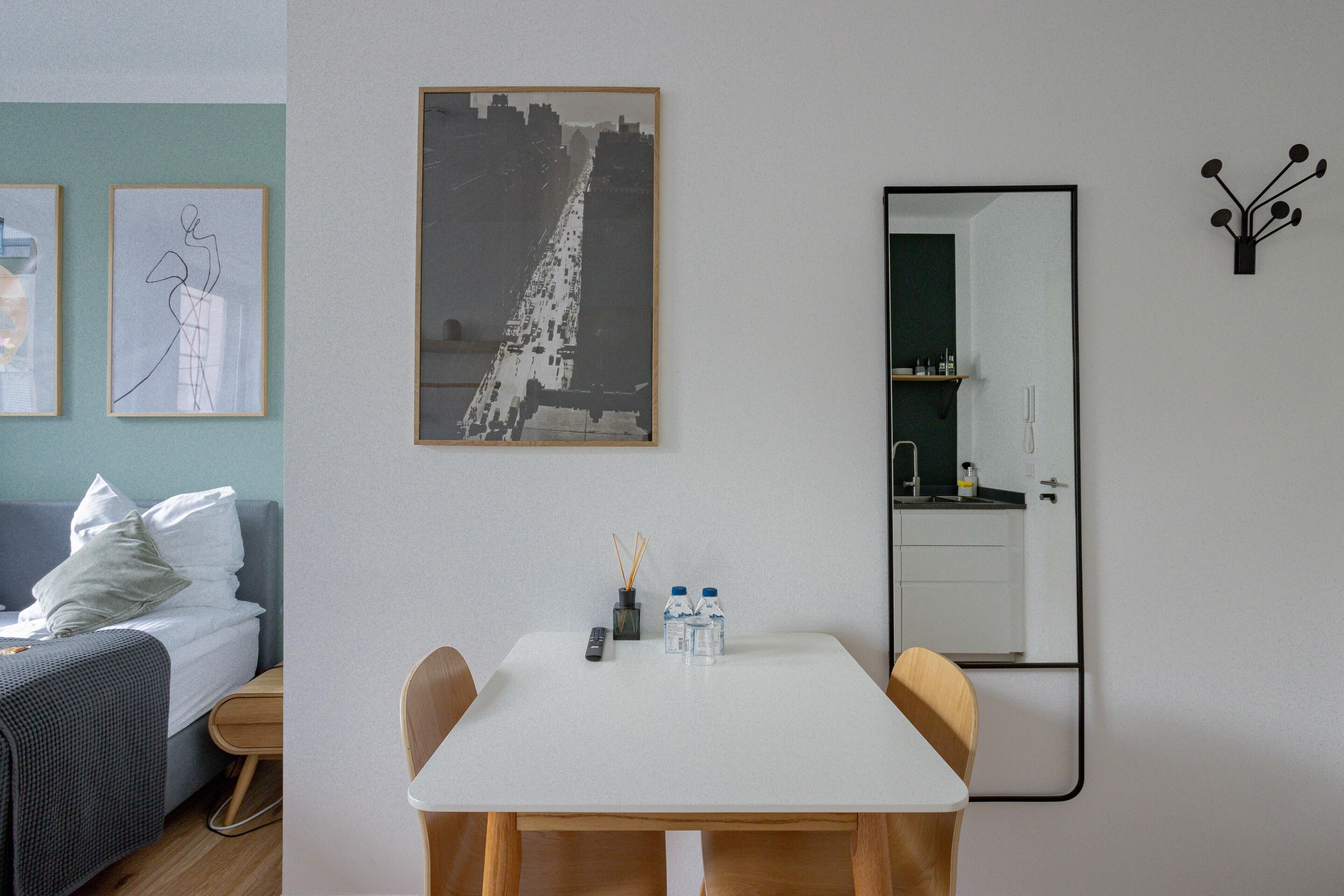 A hotel room with a bed, a dining table with chairs, a large mirror, and artwork on the walls.
