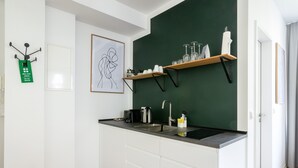 A modern kitchen with white cabinets, a black countertop, a green accent wall, and a hanging art piece.