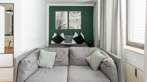 A modern bedroom with a grey sofa, a bed with grey bedding, and two framed artworks on the wall.