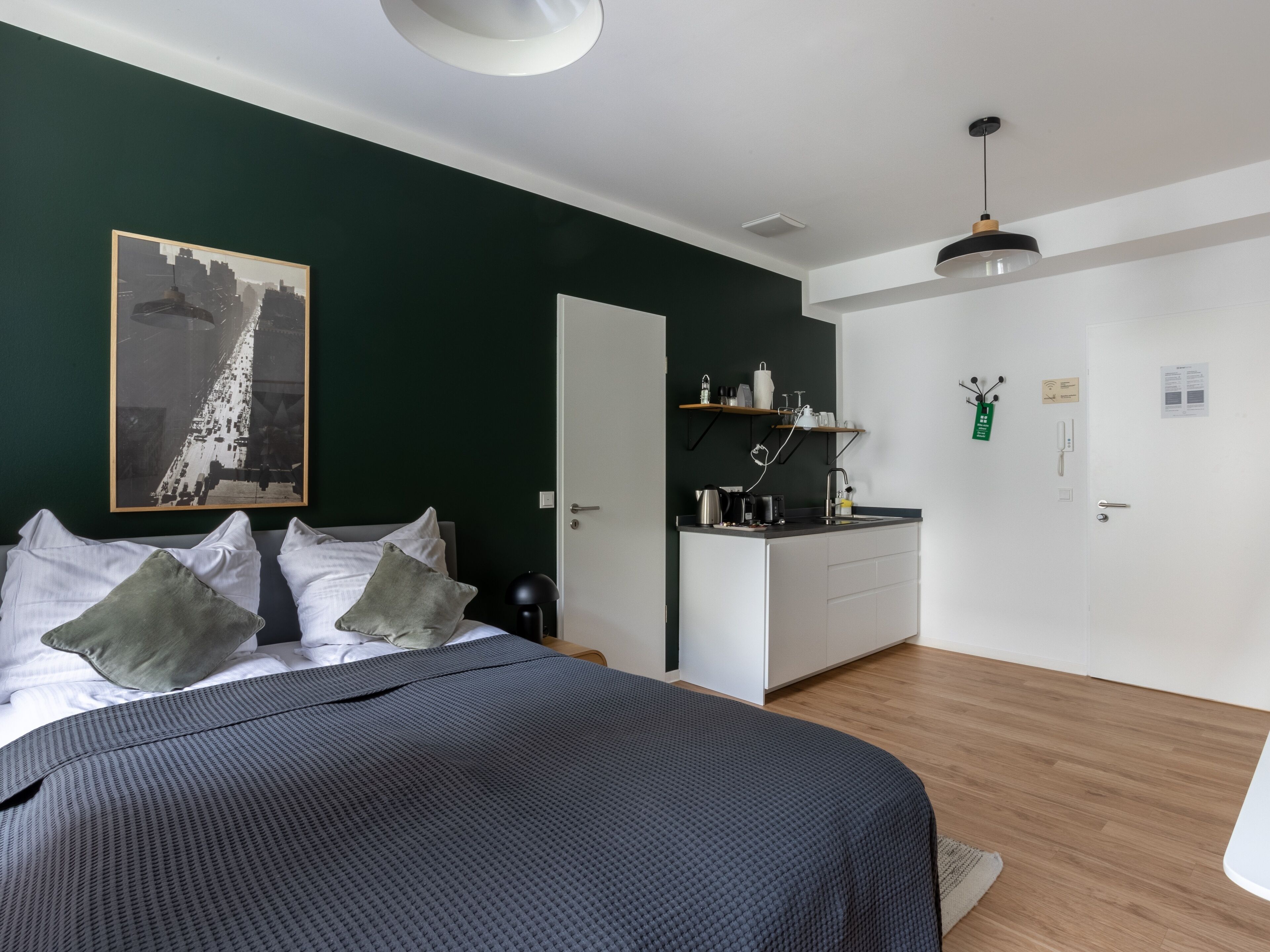 A modern bedroom with a bed, a nightstand, a desk, and a kitchen area.
