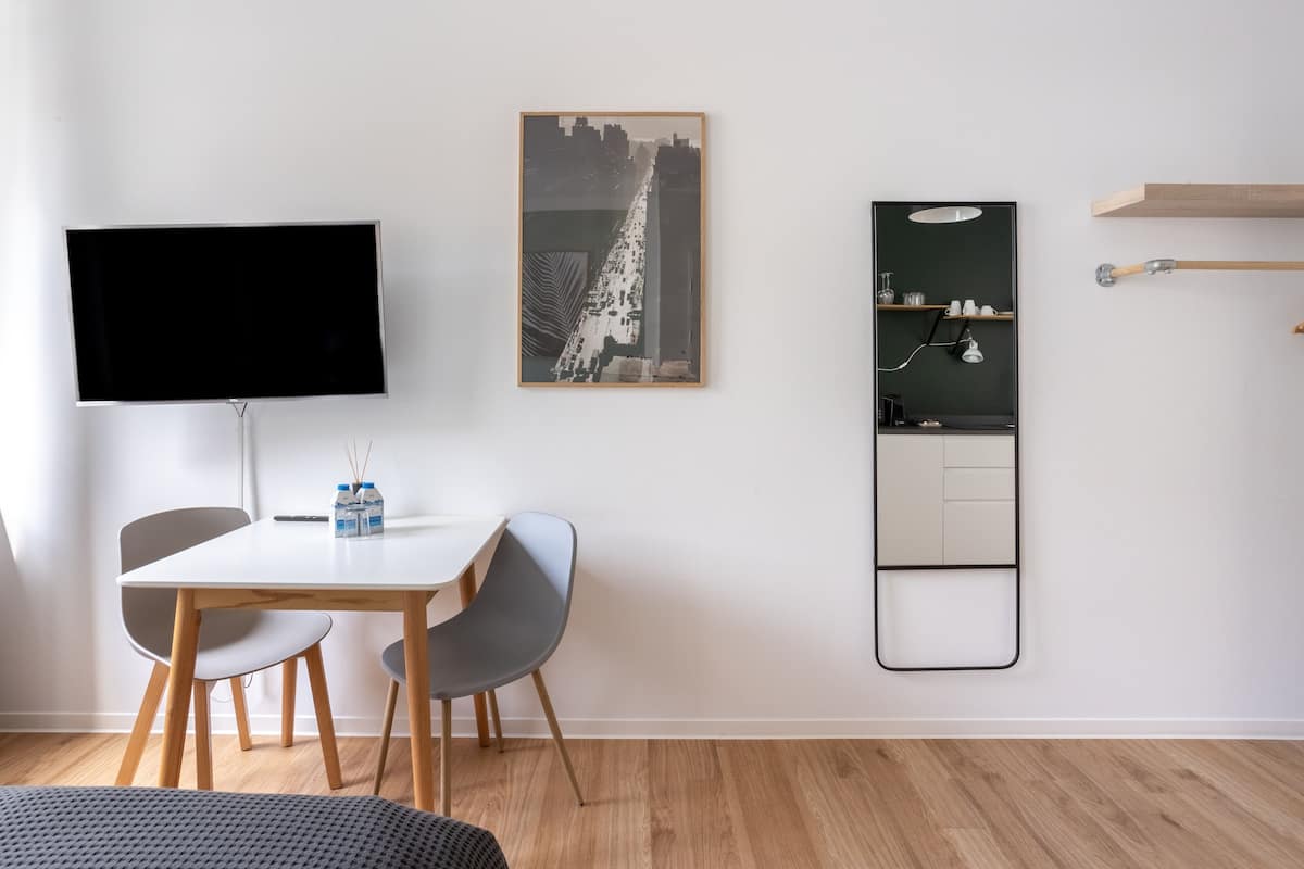 Een moderne kamer met een flatscreen televisie, een stadslandschap schilderij, een spiegel en een klein plankje met glazen.