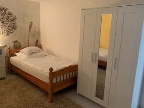 A bedroom with a wooden bed, white bedding, a nightstand, a lamp, a decorative vase, and a wardrobe with a mirror. - Apartment King (Omisalj)