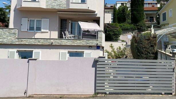 A two-story house with a balcony, a chimney, and a tall tree in the background. - Apartment King (Omisalj)