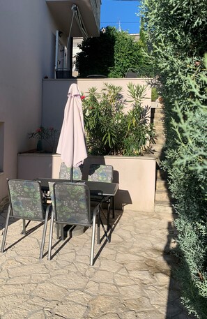 An outdoor patio with a table and chairs, surrounded by plants and a stone floor. - Apartment King (Omisalj)