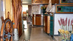 A hotel lobby with a reception desk, a wooden ship's wheel, a decorative vase with plants, and a patterned floor. - Hotel Sole (Giulianova)