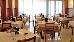 A dining area with multiple tables and chairs, arranged in rows, with a large window in the background. - Hotel Sole (Giulianova)