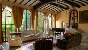 Um quarto amplo com um piano de cauda, vários espaços de estar e grandes janelas em arco.