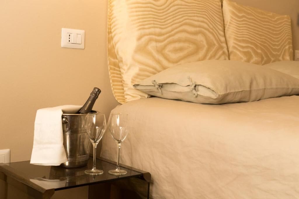 A hotel room with a bed, a nightstand, a bottle of champagne, and two wine glasses.