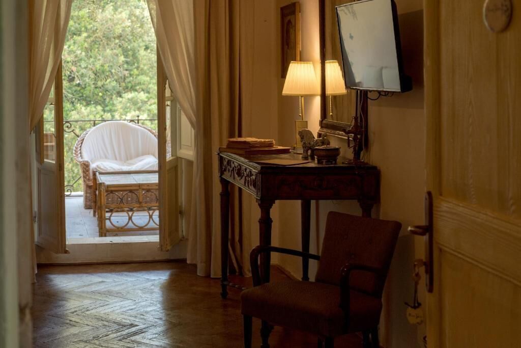 A room with a wooden floor, a desk with a lamp, a chair, a bed with a canopy, and a TV on the wall.