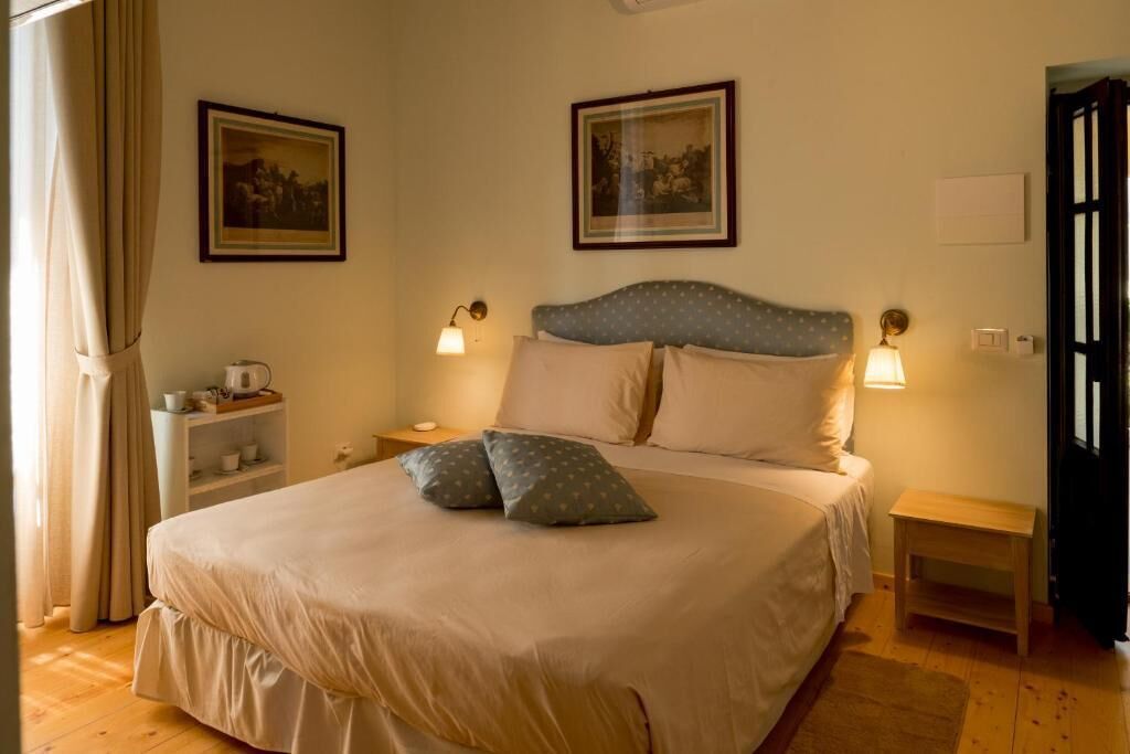Un dormitorio con una cama, mesitas de noche, un estante con tazas y cuadros en la pared.