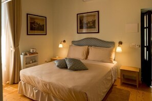 Un dormitorio con una cama, mesitas de noche, un estante con tazas y cuadros en la pared.