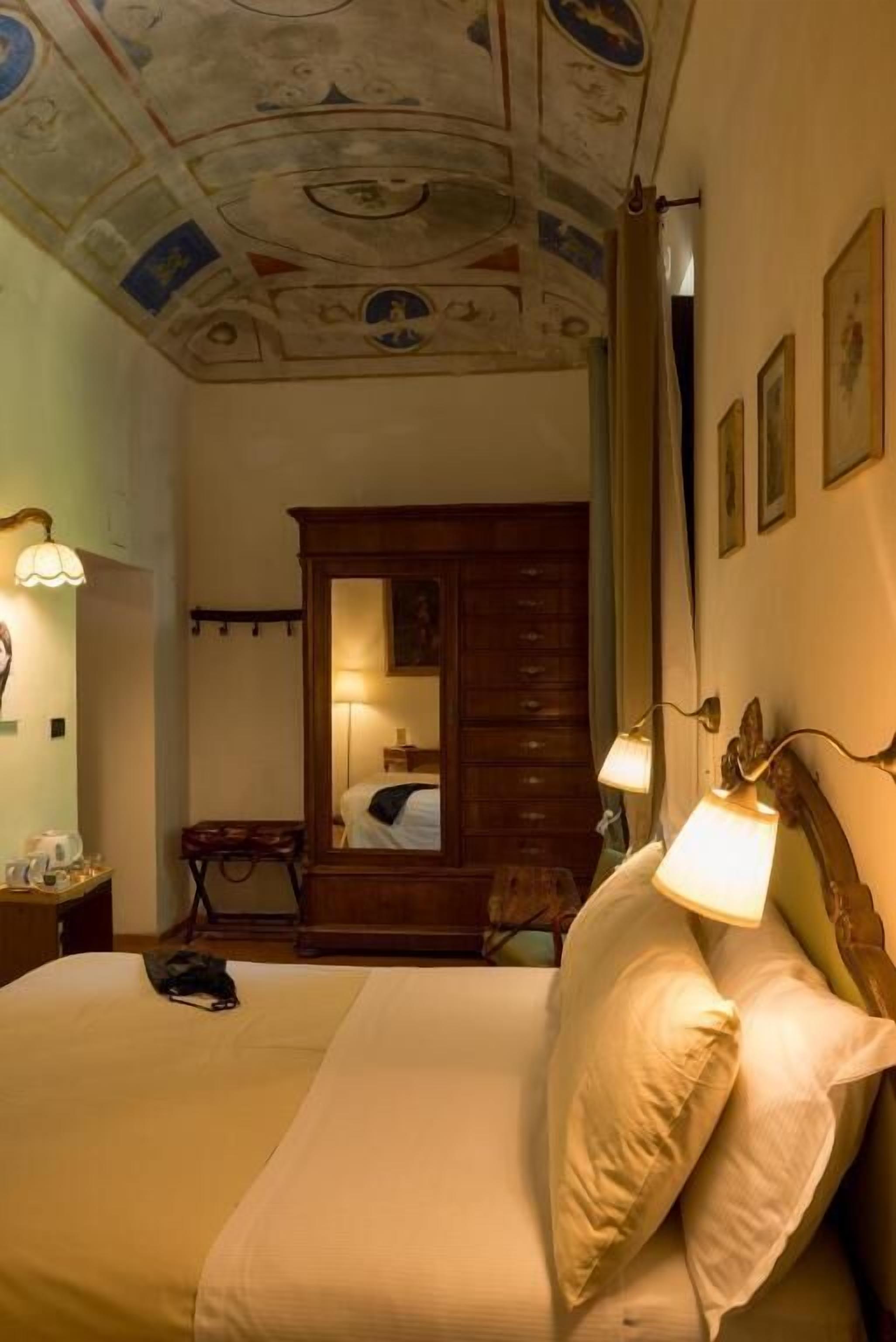 A hotel room with a bed, a nightstand, a lamp, a dresser, and a mirror.