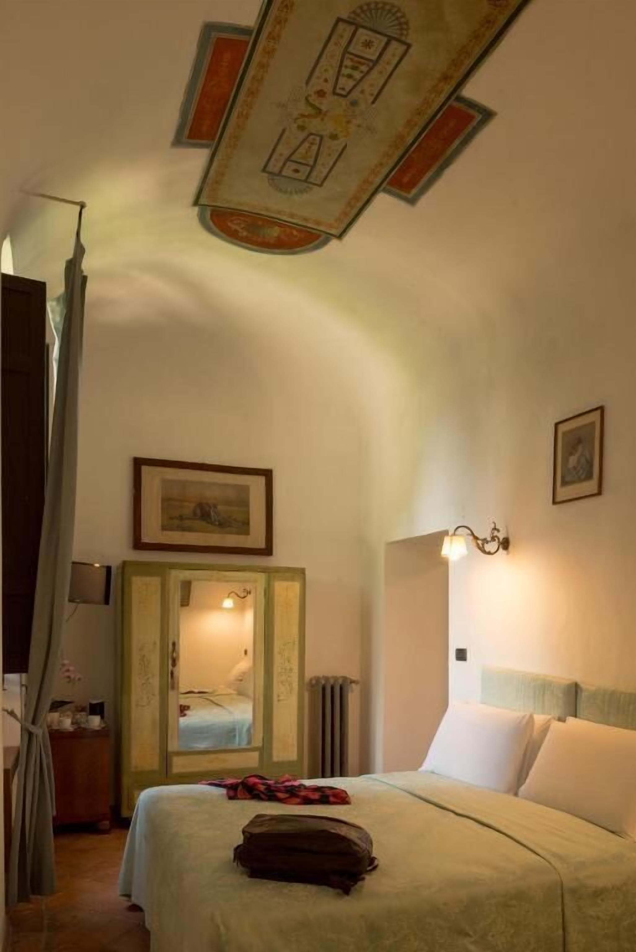 Un dormitorio con cama, armario, espejo, lámpara y una obra de arte en el techo.