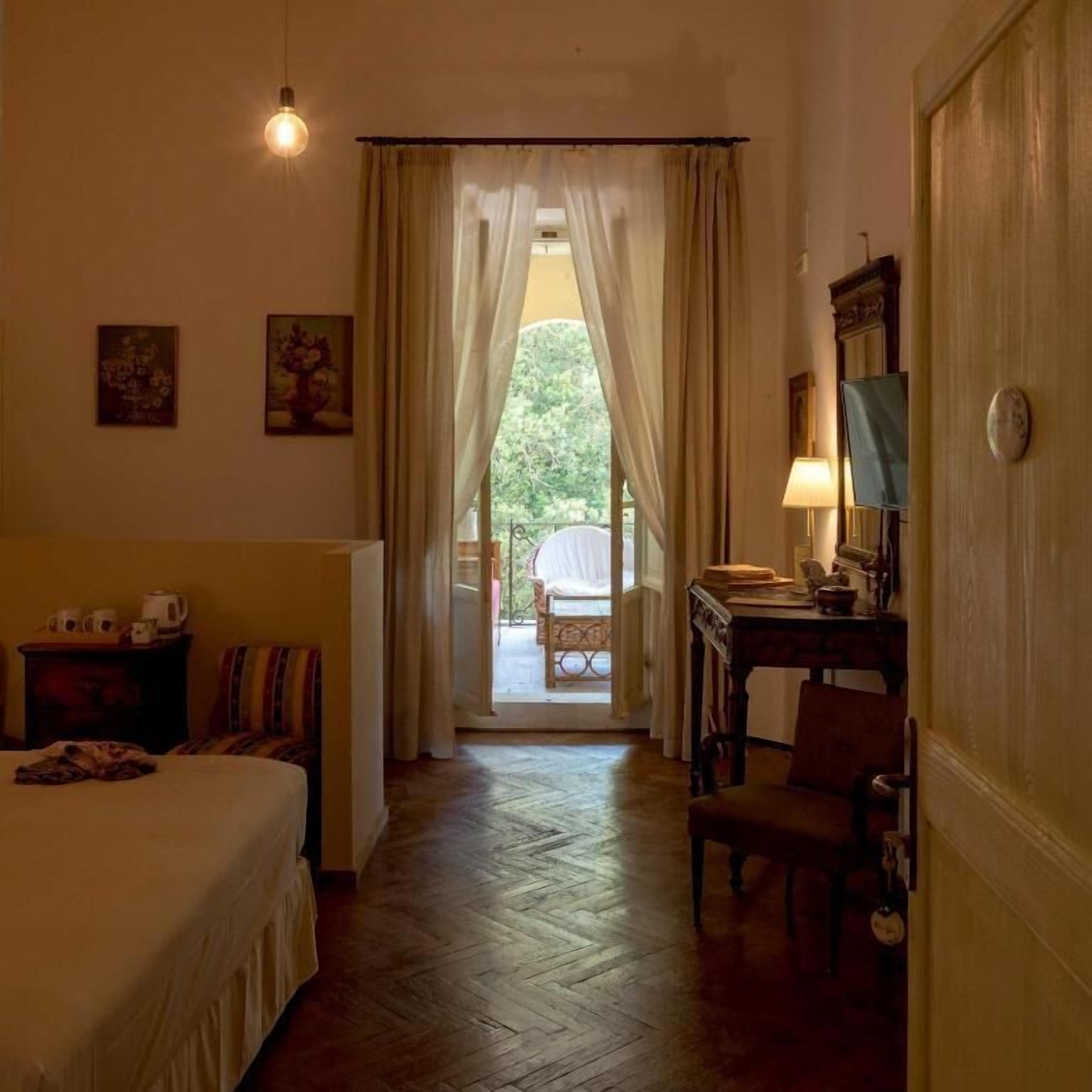 A hotel room with a bed, a desk with a lamp, a chair, and a view through a doorway.