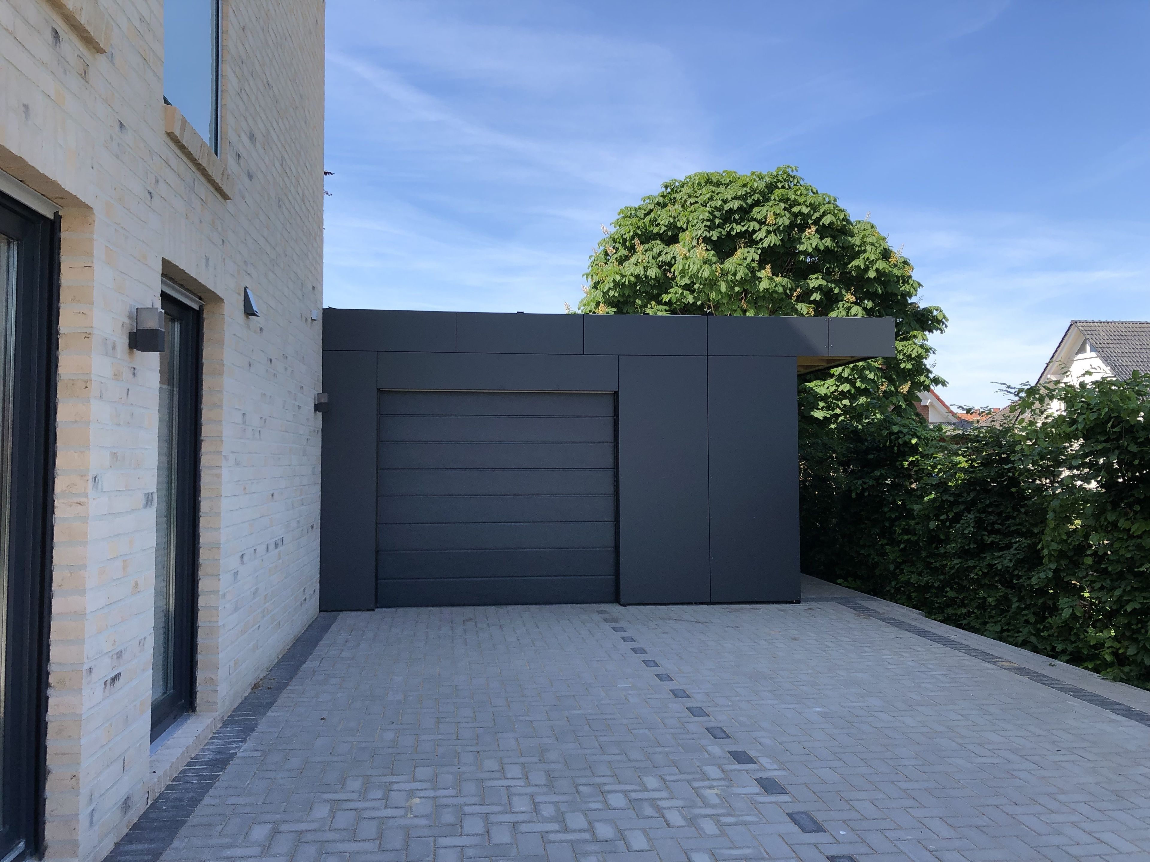 Un bâtiment moderne avec une porte de garage gris foncé, une façade en briques et une allée pavée.
