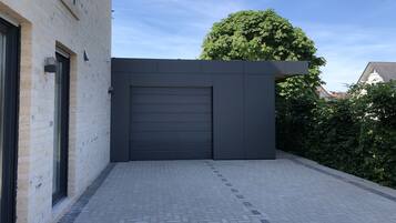 Un bâtiment moderne avec une porte de garage gris foncé, une façade en briques et une allée pavée.