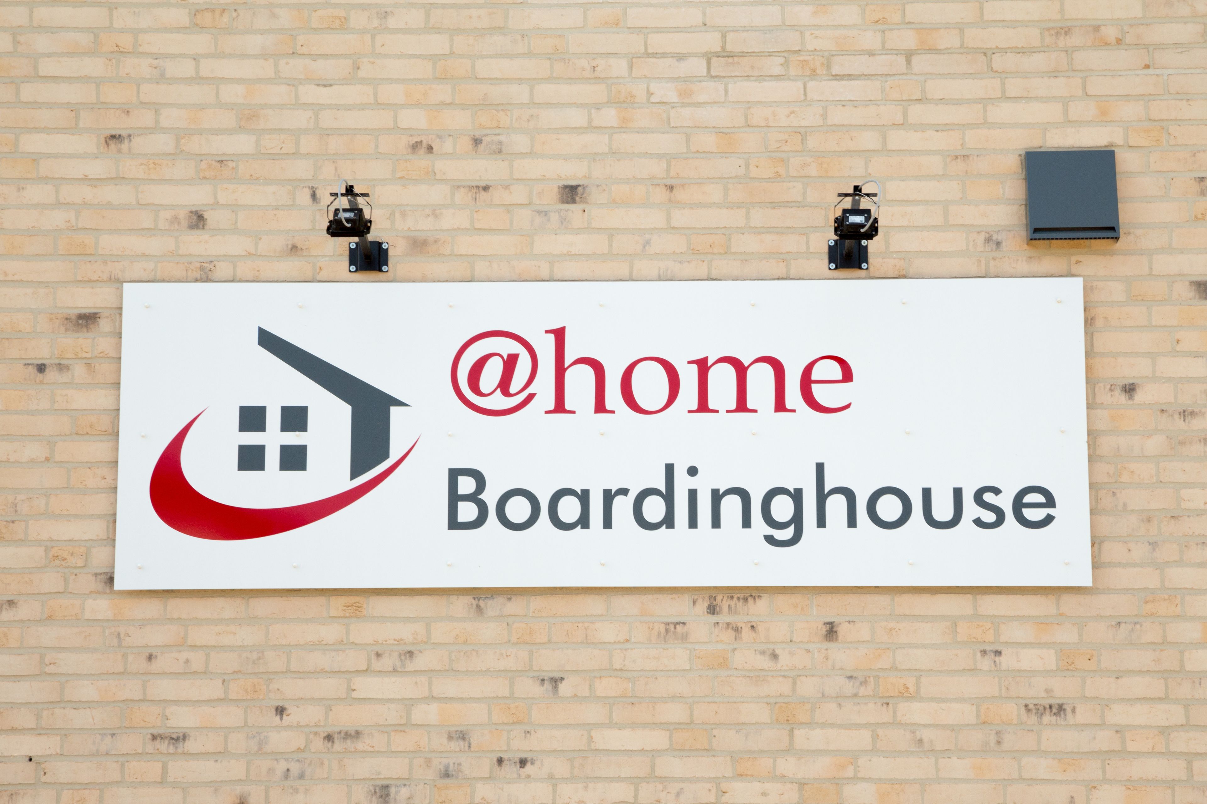 A sign for @home Boardinghouse on a brick wall.