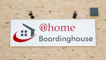A sign for @home Boardinghouse on a brick wall.