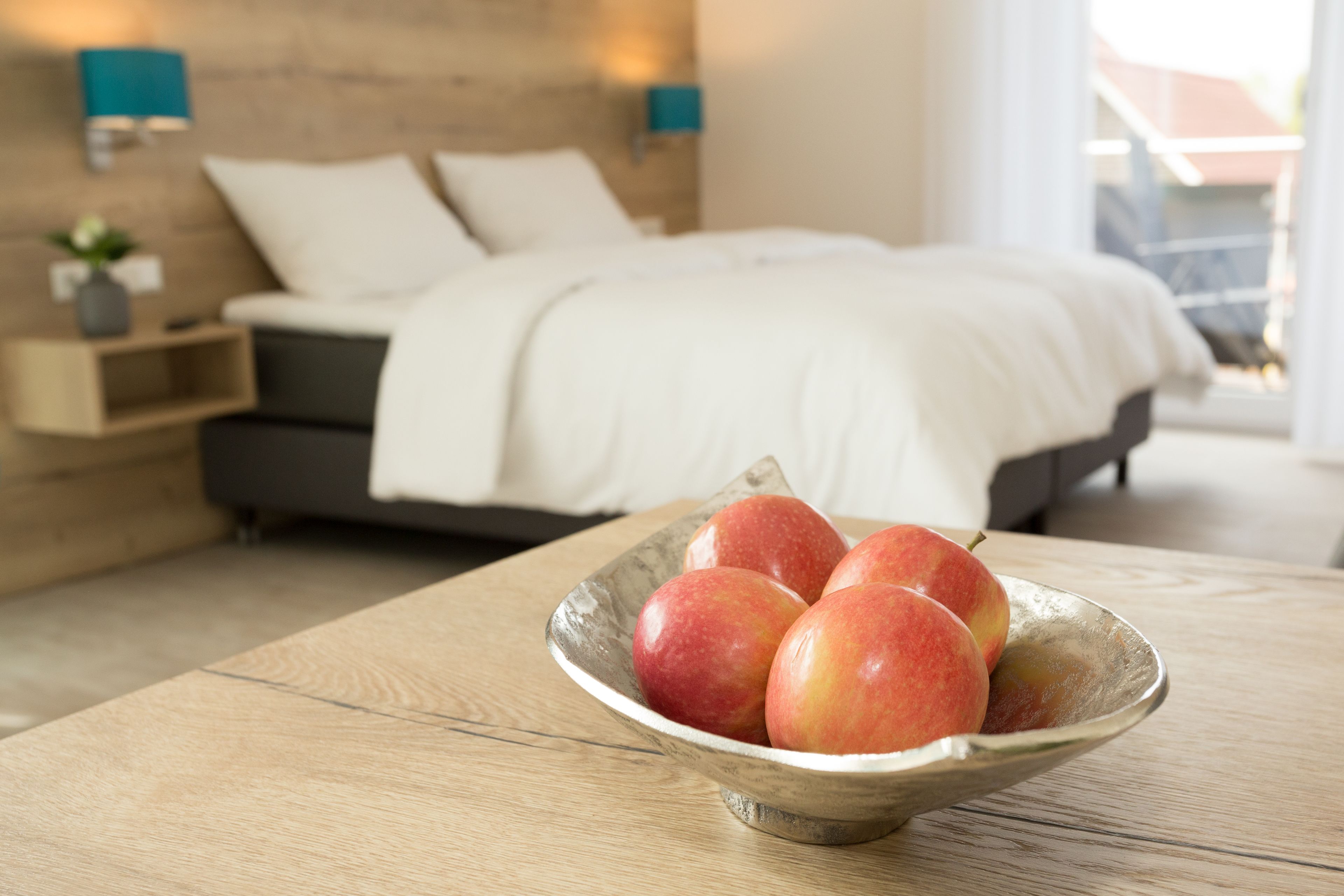 Un dormitorio con una cama, mesitas de noche y un cuenco de manzanas sobre una mesa de madera.