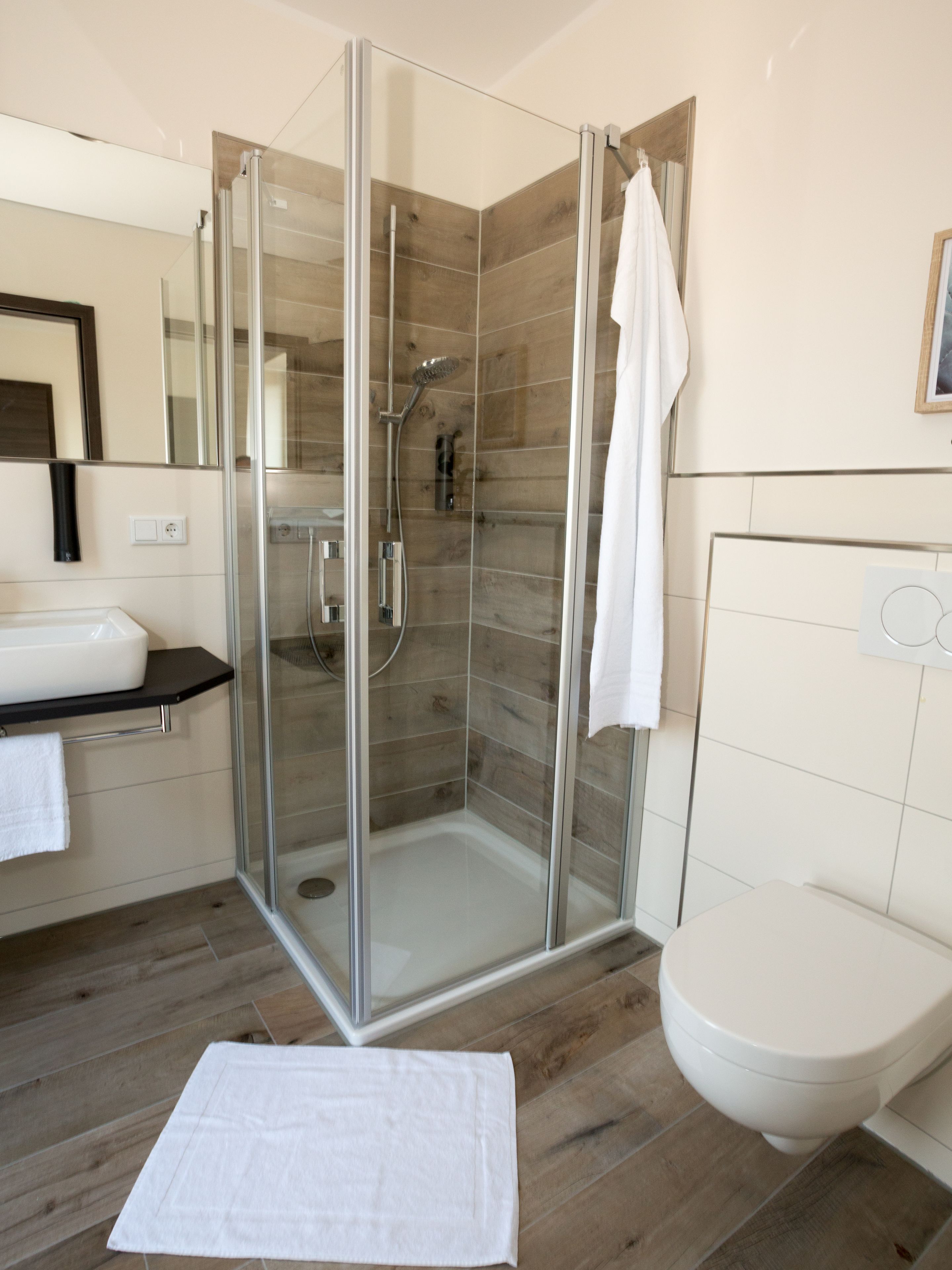 Un bany modern amb dutxa envidriada, un lavabo blanc i un vàter.