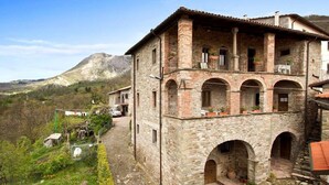 A stone building with a balcony, arched entrance, and a mountain in the background. - 3 bedroom villa (8 sleeps) with private pool in Garfagnana (55030 Villa Collemandina)