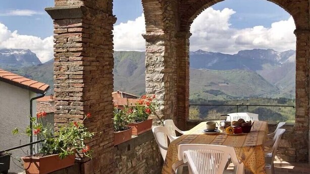 A rustic outdoor dining area with stone arches, a table set for two, and potted plants. - 3 bedroom villa (8 sleeps) with private pool in Garfagnana (55030 Villa Collemandina)
