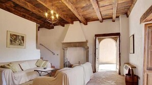 A rustic interior with a stone floor, wooden beams, a sofa, a table, and a fireplace. - 3 bedroom villa (8 sleeps) with private pool in Garfagnana (55030 Villa Collemandina)