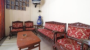 A room with a wooden table, two sofas with red and white patterned upholstery, a blue vase, and a television mounted on the wall. - Utama Syariah (Pekanbaru)