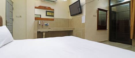Habitación de hotel con cama, un pequeño escritorio con espejo, televisor montado en la pared y puerta corredera.