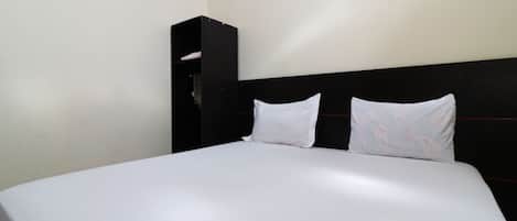 Een bed met witte beddengoed en twee kussens, een zwart hoofdeinde en een donkerhouten kast.