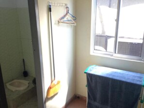 Bathroom features a toilet, broom, and clothes rack, with a window and towel in a tiled space.