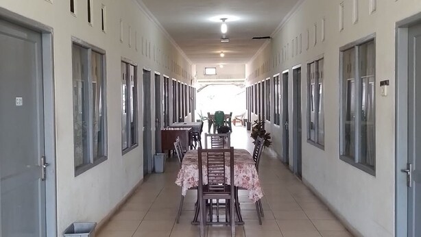A corridor with doors on both sides, a dining area with a table and chairs, and a potted plant in the foreground. - Penginapan Syariah (Pekanbaru)