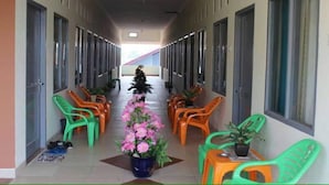 A corridor with rows of single beds, green and orange chairs, and potted plants. - Penginapan Syariah (Pekanbaru)