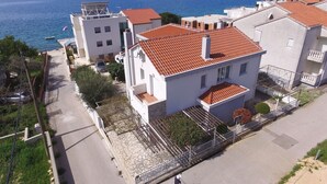 A coastal residential area with buildings featuring red-tiled roofs and white walls, a paved road, and a clear view of the sea. - Villa Adria (Zadar)