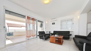 A modern living room with a sofa, chairs, and a coffee table. There is a sliding glass door leading to a balcony with a tiled roof. - Villa Adria (Zadar)