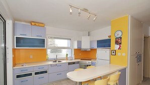 A modern kitchen with a central island, bar stools, and a yellow accent wall. - Villa Adria (Zadar)